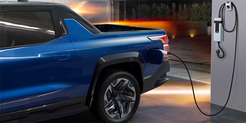 Image of a blue 2024 Chevrolet Silverado-EV parked in the garage and plugged-in to the wall, charging