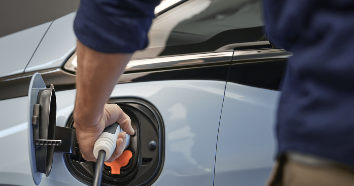 Image of a person plugging the vehicle charger to the white color EV-vehicle 